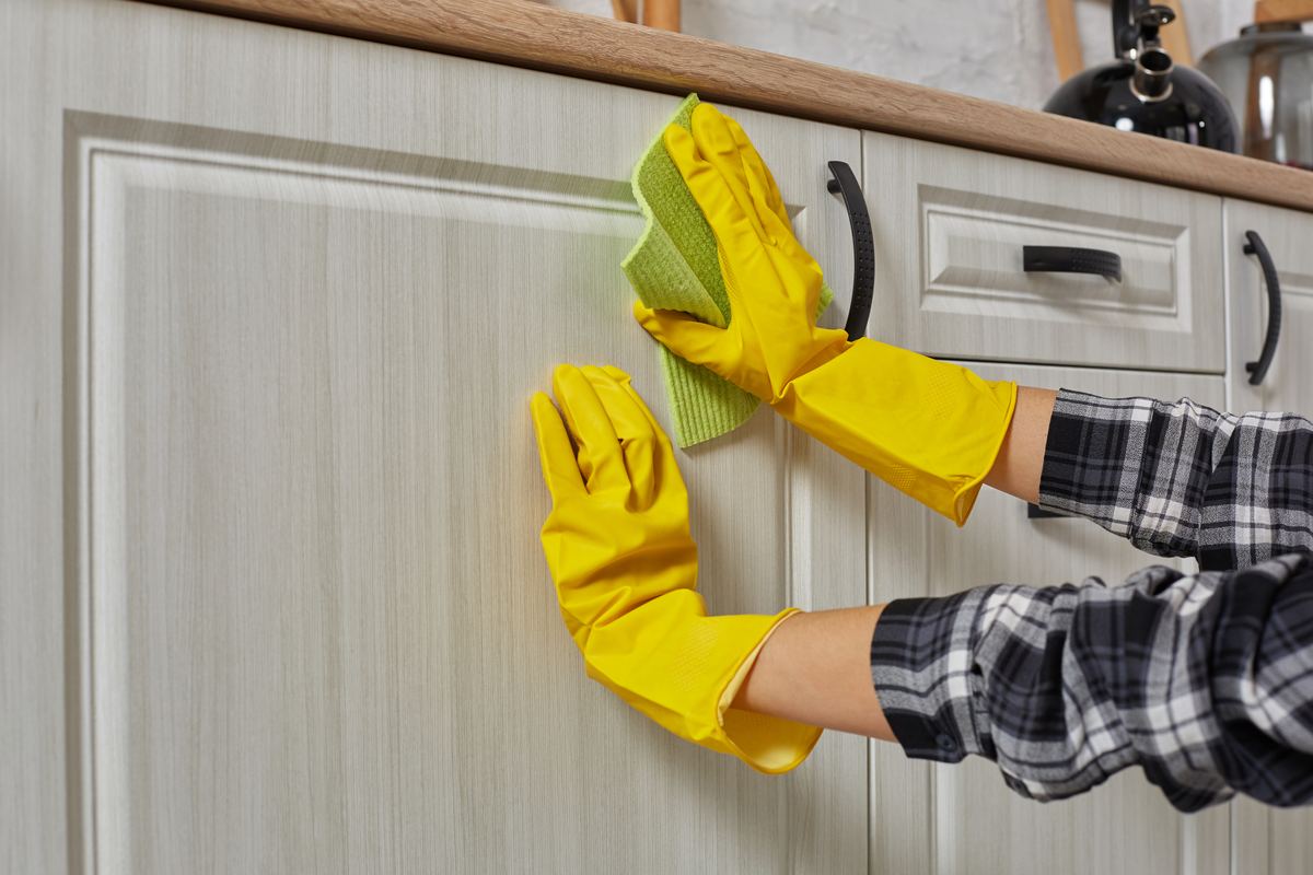 Gloved hands wiping a kitchen cabinet door during a detailed deep cleaning
